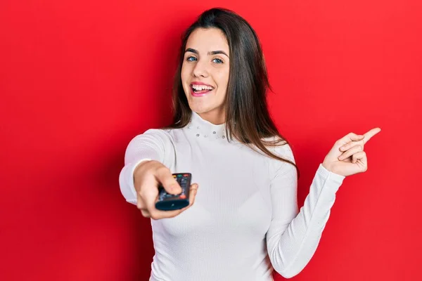 Joven Morena Adolescente Sosteniendo Control Remoto Televisión Sonriendo Feliz Señalando —  Fotos de Stock