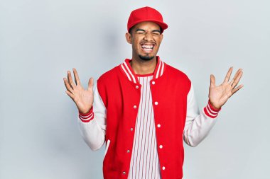 Beyzbol üniforması giyen genç Afro-Amerikan adam başarı için çıldırıyor ve çıldırıyor kollarını kaldırıyor ve gözleri kapalı heyecanla bağırıyor. Kazanan konsept 