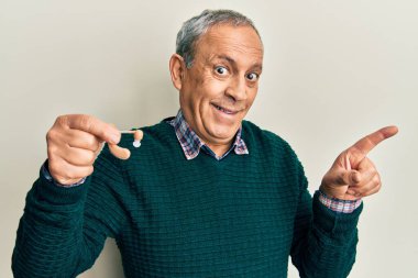 Gri saçlı, elinde tıbbi işitme cihazı olan yakışıklı bir adam gülümseyerek elini ve parmağını yana uzatarak mutlu bir şekilde işaret ediyor. 