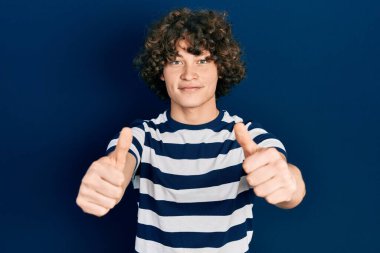 Sıradan çizgili tişört giyen yakışıklı genç adam. Elle olumlu jest yapmayı onaylıyor. Gülümsüyor ve başarı için seviniyor. kazanan jest. 