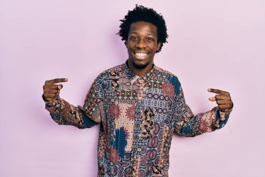 Genç Afrikalı Amerikalı sıradan kıyafetler giyen, kendine güvenen, yüzünde gülümseme olan, kendini gururlu ve mutlu gösteren bir adam.. 