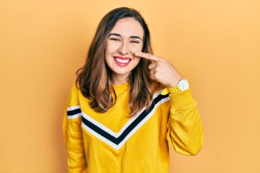 Latin asıllı genç bir kız, günlük kıyafetler giyip, el ve burnu işaret ederek, neşeli bir şekilde gülümsüyor. güzellik konsepti 