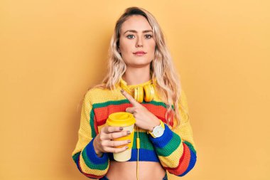 Güzel, genç, sarışın, kahve içen, kulaklık takan, el parmaklarıyla işaret eden, ciddi ve sakin bir yüz ifadesi olan bir kadın. 