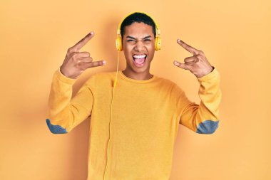 Genç Afro-Amerikalı adam müzik dinliyor kulaklıkla bağırıyor çılgın bir ifadeyle elleri havada rock sembolü yapıyor. Müzik yıldızı. ağır müzik konsepti. 