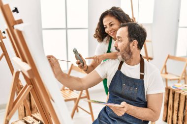 İki orta yaşlı öğrenci resim yaparken gülümsüyor ve resim stüdyosunda akıllı telefon kullanıyor..