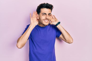 Gündelik tişört giyen genç İspanyol adam iki elini de kulak hareketlerinde duymaya çalışıyor, dedikoduya meraklı. İşitme sorunu, sağır 