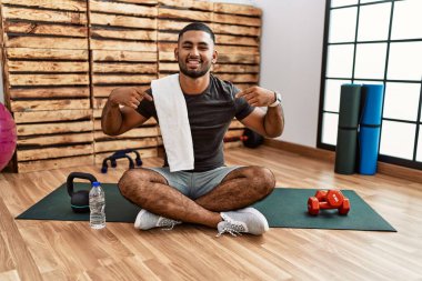 Spor salonundaki antrenman minderinde oturan genç Hintli adam kendine güvenen, yüzünde gülümsemeyle kendini gururlu ve mutlu bir şekilde gösteren.. 