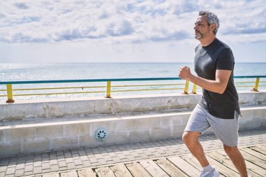 Orta yaşlı İspanyol adam spor giyer, deniz kenarında koşar.