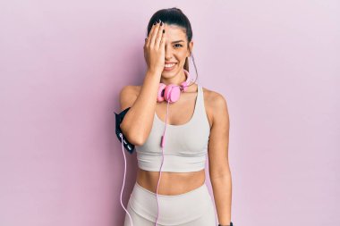 Genç İspanyol kadın spor kıyafetleri giyiyor ve kulaklık takıyor. Bir gözünü eliyle kapatıyor. Yüzünde kendine güvenen bir gülümseme ve şaşırtıcı bir duygu var.. 