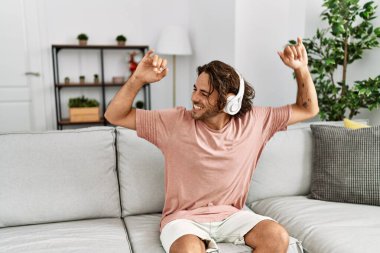 Genç İspanyol adam müzik dinliyor ve dans ediyor. Evdeki kanepede oturuyor..