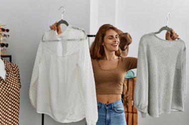 Genç beyaz kadın gülümseyerek giyim mağazasından kıyafet seçiyor..