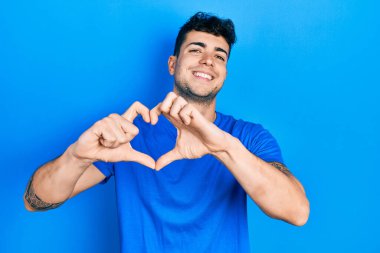 Gündelik mavi tişört giyen, aşık gülümseyen, elleriyle kalp sembolü yapan genç İspanyol adam. romantik kavram. 