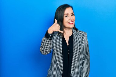 Orta yaşlı İspanyol kadın iş kıyafetleri içinde gülümsüyor telefonla el ve parmak hareketleri yapıyor telefonda konuşuyor gibi. iletişim kavramları. 