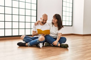 Genç İspanyol çift gülümsüyor boş evde mutlu bir kitap okuyor..