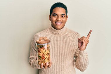 Genç, yakışıklı, İspanyol bir adam elinde makarna kavanozuyla mutlu bir şekilde gülümsüyor. 