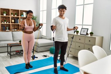 Young latin couple smiling happy training using elastic band at home.