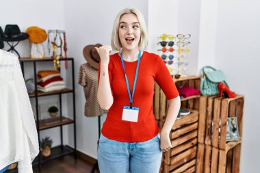 Perakende mağazasında yönetici olarak çalışan genç beyaz bir kadın gülümseyen bir yüzle yan tarafa bakıyor ve başparmağıyla işaret ediyor.. 