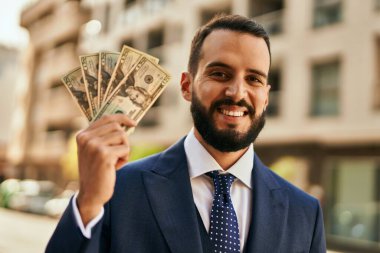 Genç işadamı gülümseyerek şehirde dolarları tutuyor..