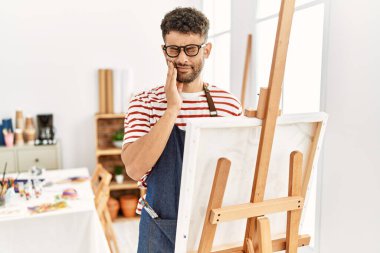 Sanat stüdyosundaki Arap genç adam diş ağrısı ya da diş hastalığından dolayı acı dolu bir ifadeyle ağıza dokunuyor. dişçi kavramı. 