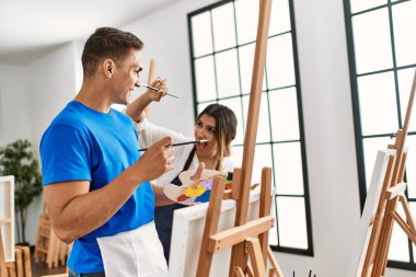 Resim okulunda boya fırçasıyla oynarken gülümseyen iki öğrenci..