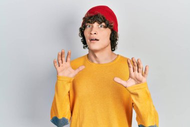 Yün şapka takan yakışıklı genç adam korku ifadesinden korkmuş ve dehşete düşmüş. El kol hareketi yapmayı kes, şok içinde bağır. panik konsepti. 