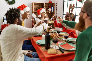 Bir grup genç, mutlu bir şekilde gülümseyerek evde Noel yemeği yiyor..