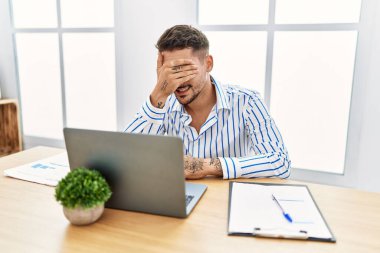 Ofiste çalışan sakallı yakışıklı genç bir adam bilgisayarda çalışırken gülümseyen ve gülen elleri yüzüyle şaşkınlıktan gözleri kapatıyordu. kör kavram. 