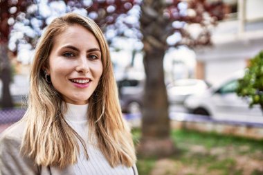 Parkta kendinden emin gülümseyen genç sarışın kadın.