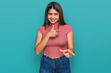 Günlük tişört giyen genç İspanyol kız mutlu ve komik yüzlü parmaklarını kameraya doğrultuyor. iyi enerji ve titreşimler. 