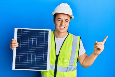 Fotovoltaik güneş paneli tutan yakışıklı genç adam gülümsüyor. 