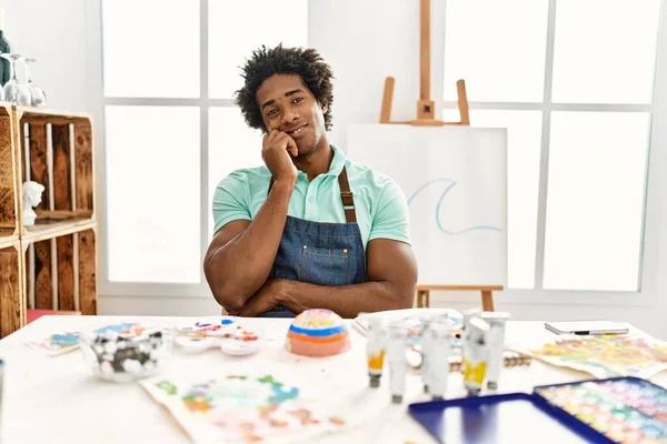 若いアフリカ系アメリカ人の男座っているテーブルの上にアートスタジオ考え疲れていると退屈でうつ病の問題で交差腕 — ストック写真