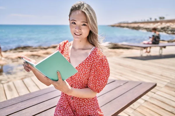 Genç Çinli Kız Gülümseyerek Sahilde Mutlu Bir Şekilde Kitap Okuyor — Stok fotoğraf