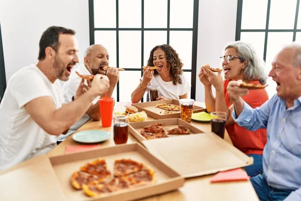 Group of middle age people smiling happy eating italian pizza sitting on the table at home