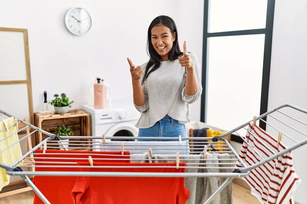 若いヒスパニック系の女性が幸せと面白い顔でカメラに指を指して服の上に新鮮な洗濯を入れて 良いエネルギーと振動は — ストック写真