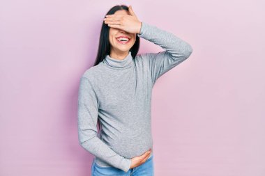 Mavi gözlü güzel bir kadın bebek bekliyor, hamile karnına dokunuyor gülümsüyor ve elleri yüzünde şaşkınlık için gözleri örtüyor. kör kavram. 