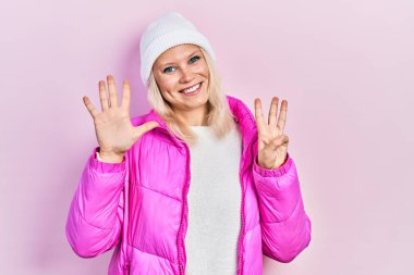 Kafkasyalı güzel sarışın kadın yün şapka takıyor ve kışlık ceket giyiyor. Sekiz numaralı parmaklarıyla işaret ediyor ve gülümsüyor. Kendinden emin ve mutlu.. 