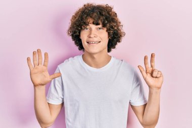 Yakışıklı, beyaz tişört giyen, 8 numaralı parmaklarıyla gösteriş yapan, kendine güvenen ve mutlu bir genç.. 