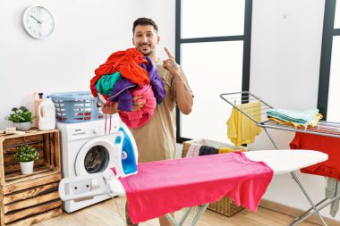 Çamaşırları tutan yakışıklı genç adam mutlu ve gururlu gülümseyen birini işaret etmeye hazır. 