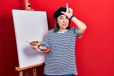 Orta yaşlı İspanyol bir kadın boyacı sehpası ile resim çiziyor parmakları alnında insanlarla dalga geçiyor ezikçe davranışlar sergiliyor ve aşağılıyor.. 