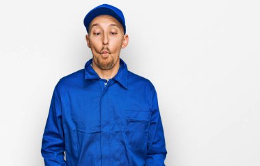 Sakallı, inşaatçı tulumu giymiş kel bir adam dudaklarıyla balık suratı yapıyor, çılgınca ve komik bir jest. Komik ifade. 