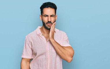 Sakallı, sıradan tişörtlü, diş ağrısı ya da diş hastalığından dolayı acı dolu bir ifadeyle dudaklarına dokunan İspanyol bir adam. dişçi 