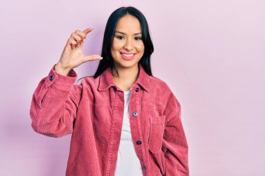 Güzel İspanyol kadın, burun piercingli, sıradan pembe ceketli, gülümseyen, kendine güvenen, el hareketleriyle küçük boy işareti yapan, parmaklarıyla bakan ve kamerasıyla. ölçüm kavramı. 