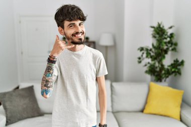 Oturma odasında sakallı, gülümseyen, el ve parmaklarıyla telefonla konuşan İspanyol bir adam. iletişim kavramları. 