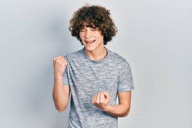 Gri bir tişört giyen yakışıklı genç adam kolları havada ve gözleri kapalı bir şekilde başarıyı kutluyor. 