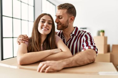 Genç beyaz çift mutlu bir şekilde gülümsüyor. Yeni evlerinde karton kutuya yaslanıyorlar..