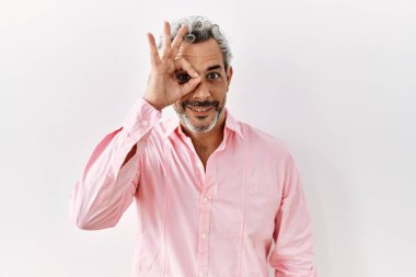 Orta yaşlı İspanyol bir adam tecrit edilmiş arka planda duruyor. El hareketleriyle gülümsüyor, gözleriyle gülen parmaklarının arasından bakıyor.. 