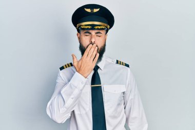 Uçak pilotu üniforması giyen genç İspanyol adam ağzıyla esnemekten sıkılmış. Huzursuz ve uykulu.. 