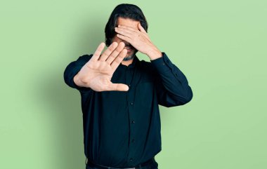 Orta yaşlı beyaz bir adam, günlük kıyafetler ve gözlük takıyor, gözleri ellerle örtüyor ve üzgün ve korku ifadeleriyle jestleri durduruyor. utangaç ve olumsuz kavram. 