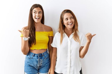 Anne ve kızı yalıtılmış arka planda bir arada mutlu yüzle gülümsüyor ve baş parmağıyla yan tarafı işaret ediyor.. 