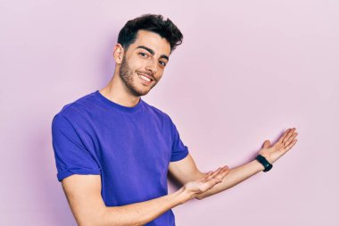 Gündelik tişört giyen genç İspanyol adam gülümseyerek içeri girmeye davet ediyor. 